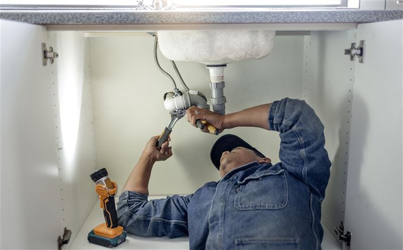 Plumber repairing pipes beneath a bathroom sink in Sacramento